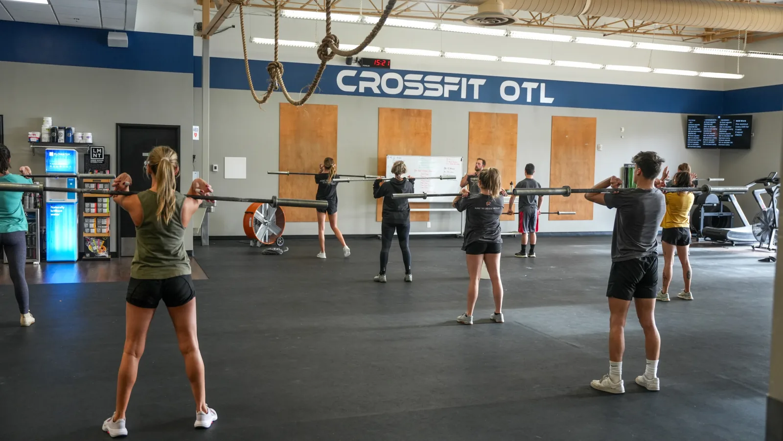A CrossFit OTL class practicing a lift with empty barbells